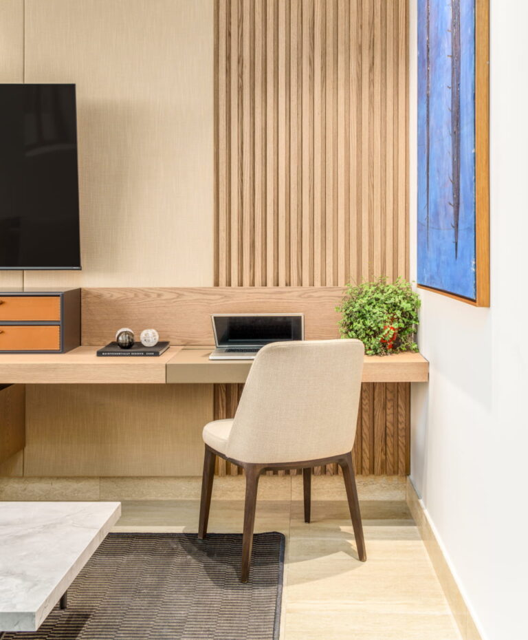 Espacio de estudio con escritorio en madera, silla tapizada y panel decorativo, junto a TV en The Woods Santa María.